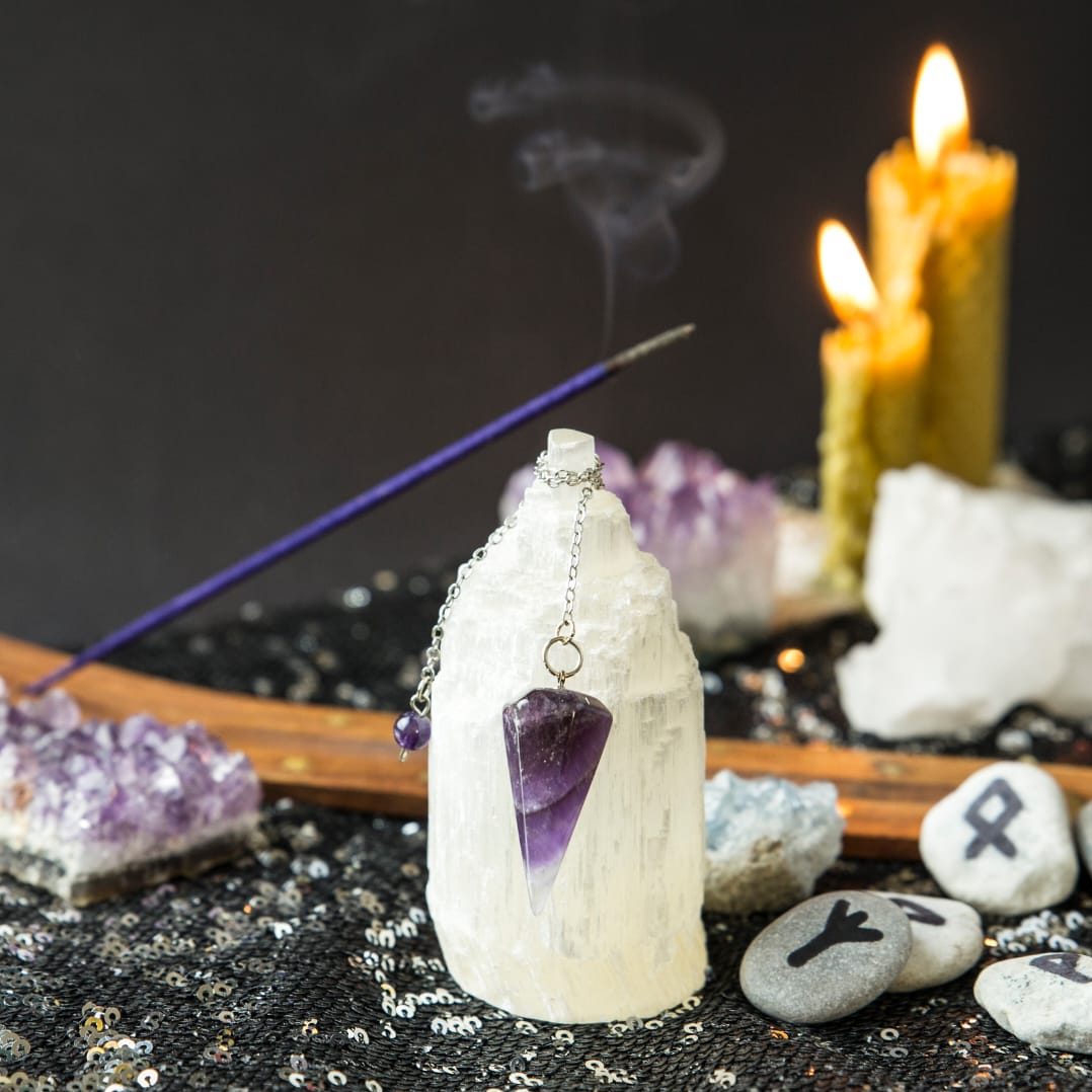 Crystals, candles in the background, pendulum